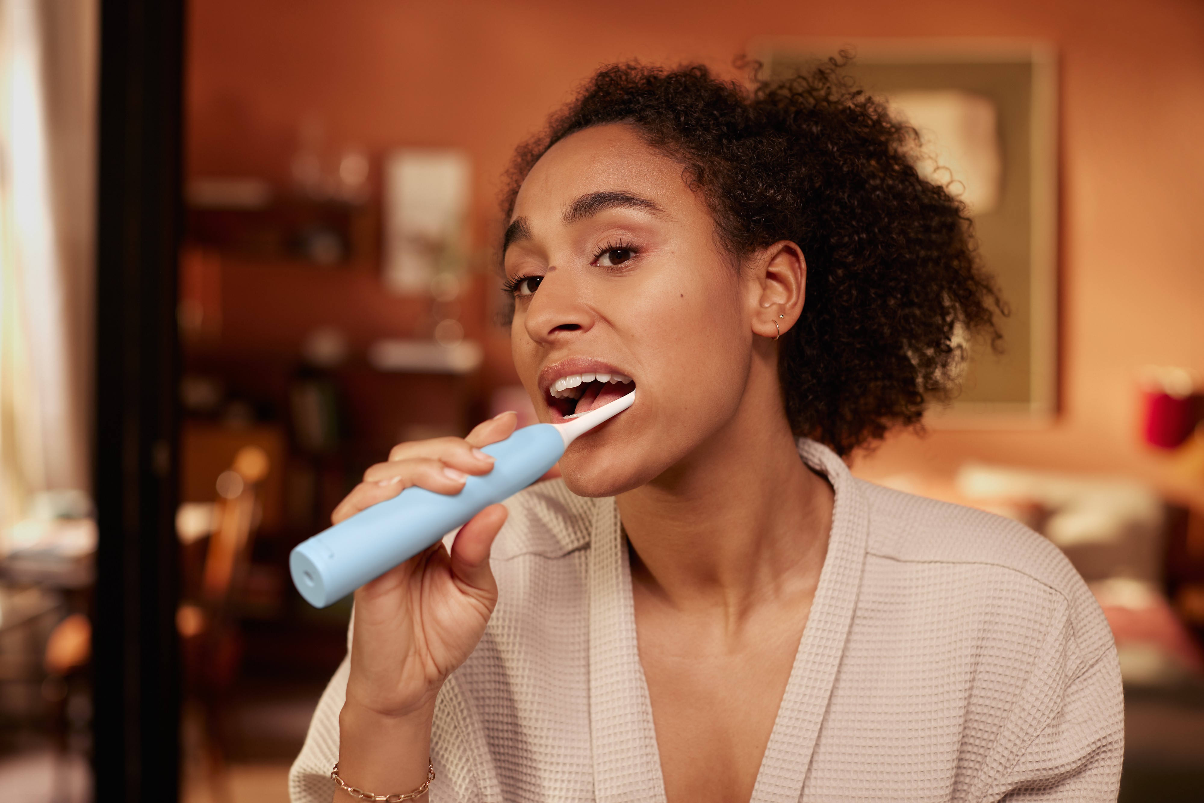 A young woman is using a light blue Philips electric toothbrush to brush her teeth and avoid coated and white tongue issues.
