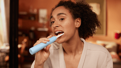 A young woman is using a light blue Philips electric toothbrush to brush her teeth and avoid coated and white tongue issues.