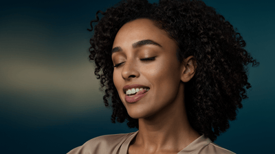 A young woman smiles as she licks her white teeth against a dark gradient background.
