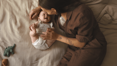 A woman spends quality time with her young baby on a bed while wearing a Philips Avent Wearable Breast Pump.