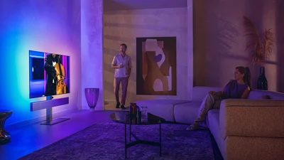 Man en vrouw in een stijlvolle woonkamer kijken naar een Philips Ambilight-tv waarop een cello-optreden wordt getoond