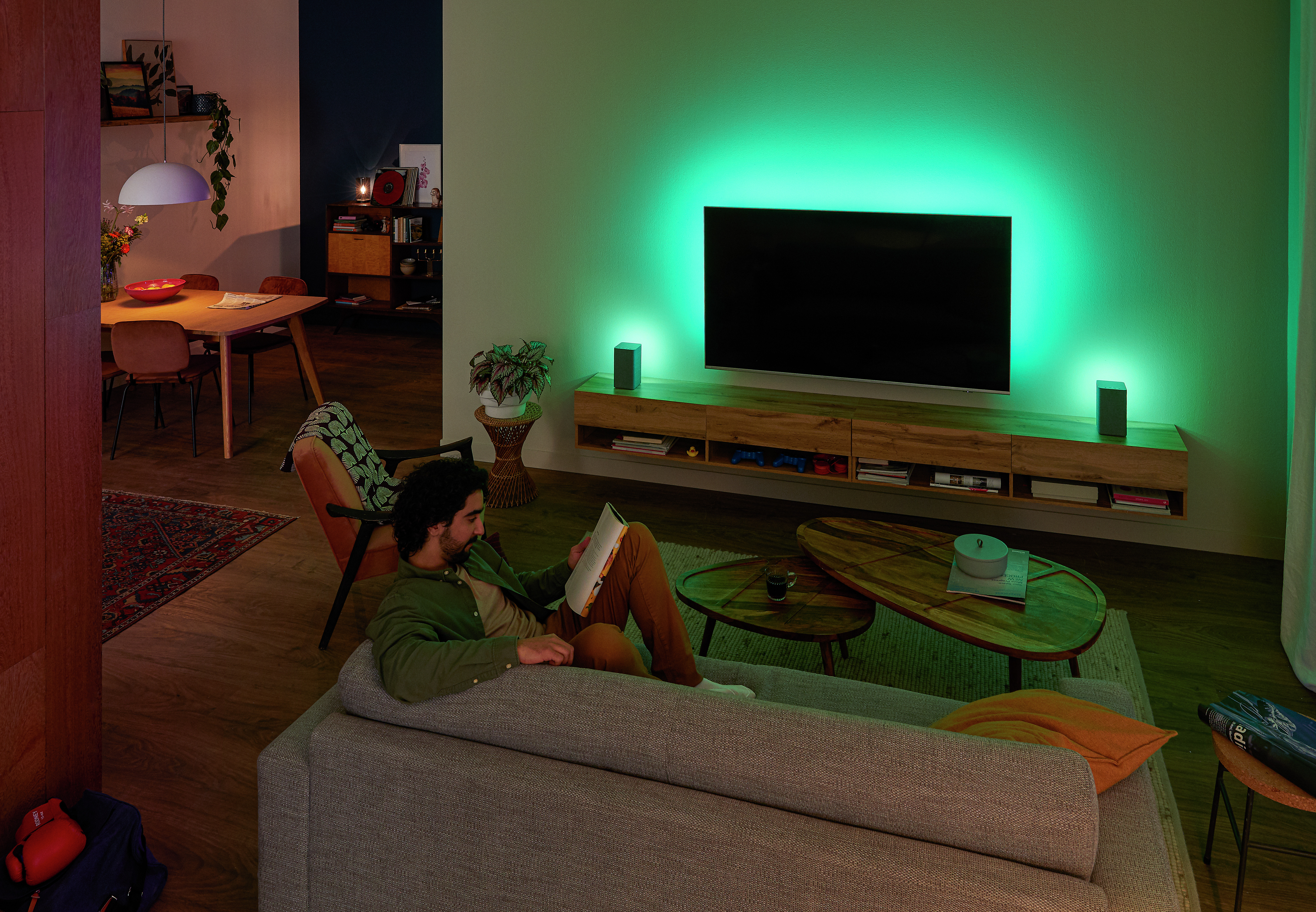 Osoba relaxuje na pohovke s televízorom Philips Ambilight, zelené ambientné svetlo osvetľuje stenu.