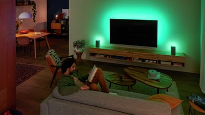 Osoba se opušta na kauču uz Philips Ambilight TV, zeleno ambijentalno svjetlo osvjetljava zid.