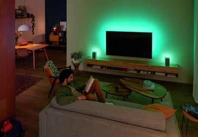 Person entspannt auf einem Sofa mit einem Philips Ambilight Fernseher, grünes Ambient-Licht erhellt die Wand.