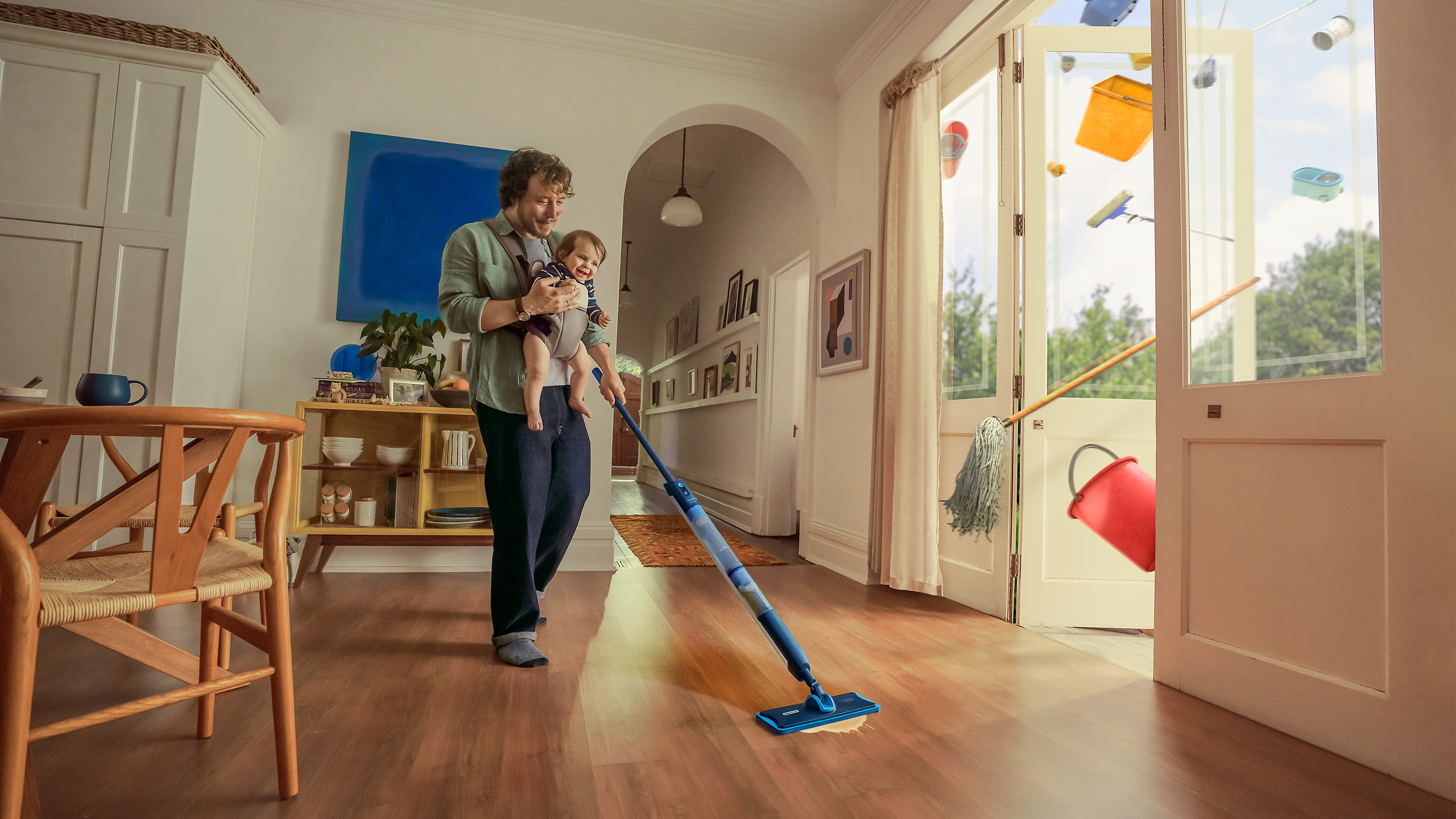 Мъж, държащ бебе, който почиства дървен под с мопа в светла