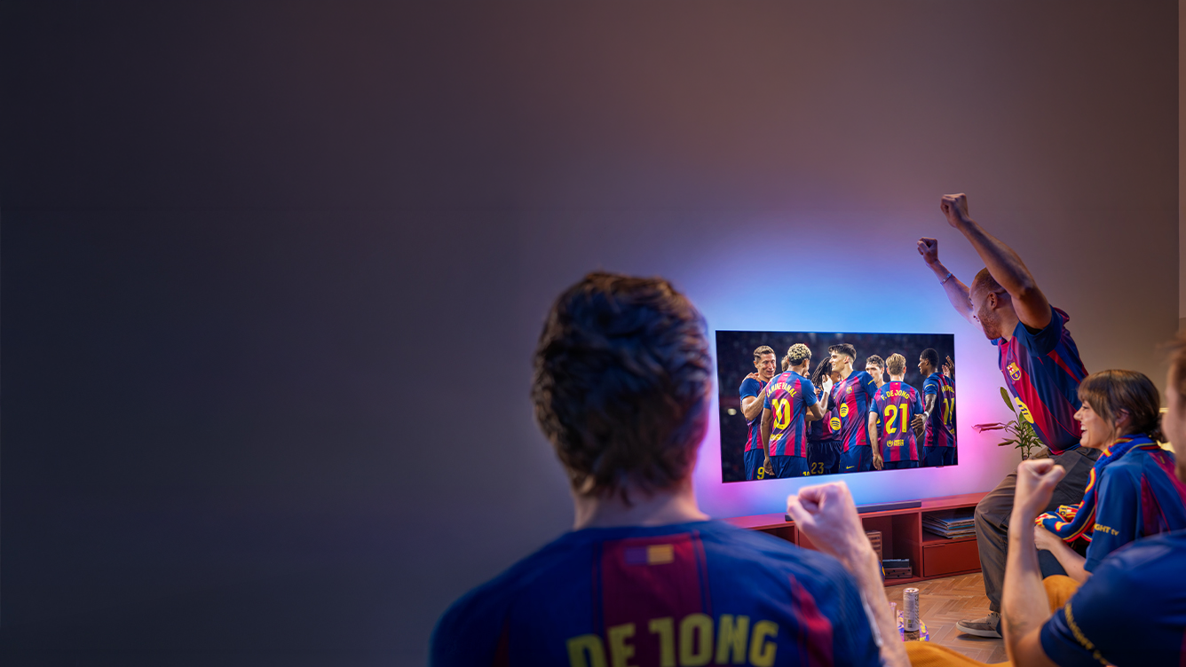 Skupina fanúšikov v dresoch FC Barcelona fandí pri sledovaní zápasu FC Barcelona na televízore Philips Ambilight so svietiacim farebným osvetlením