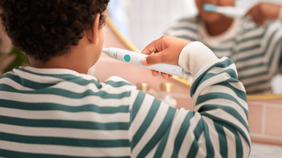 Un bambino si lava i denti davanti allo specchio.