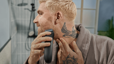 Un uomo biondo con un tatuaggio di un uccello sul collo si sta radendo la barba con Philips OneBlade.
