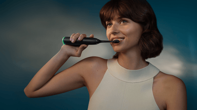 Eine Frau putzt sich mit einer elektrischen Philips Next-Generation DiamondClean Zahnbürste die Zähne und lächelt.