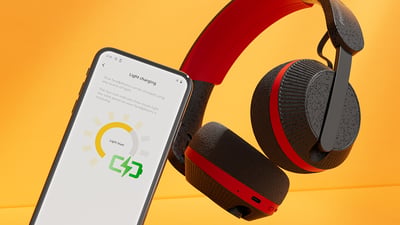 Cuffie Philips A6219 accanto a uno smartphone che mostra la schermata di ricarica luminosa, su uno sfondo arancione brillante