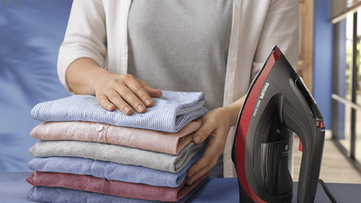 Hände, die Kleidung mit einem Bügeleisen falten