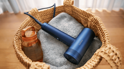 Eine Nahaufnahme eines Philips Haartrockners der Serie 8000 in einem mit blauem Handtuch ausgelegtem Weidenkorb.