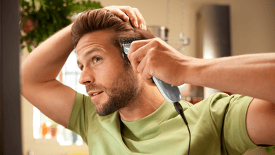A man is using Philip hair clippers to shave and style the left side of his head into a buzz cut.