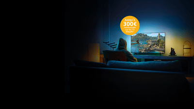 Personne jouant à Assassin’s Creed sur un téléviseur Philips Ambilight dans un salon faiblement éclairé, illuminé par les effets immersifs d’Ambilight.