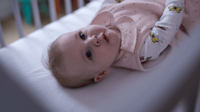 A young infant lies peacefully in a wooden cot.