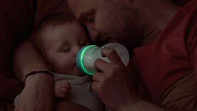 A close-up shot of a man holding his baby while feeding them with a Philips Natural Response Nighttime bottle.