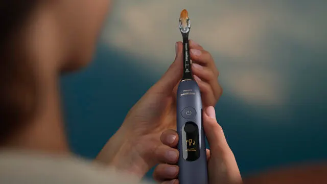 A woman holds a navy blue Philips Next-Generation DiamondClean electric toothbrush in her hands.