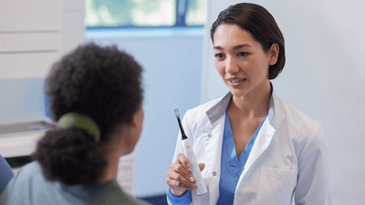A young dental professional holds a black and white Philips electric toothbrush to her patient while explaining the signs of pregnancy gingivitis.