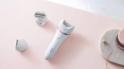 A product image of a Philips epilator and attachments on a light pink table.
