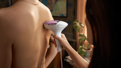 A woman using her pink Philips IPL Lumea machine on a man's back.