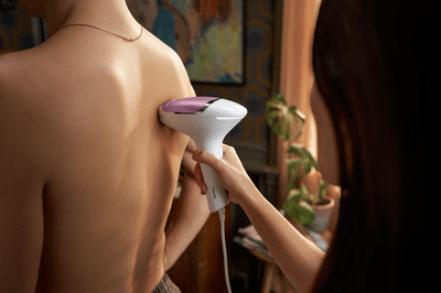 A woman using her pink Philips IPL Lumea machine on a man's back.