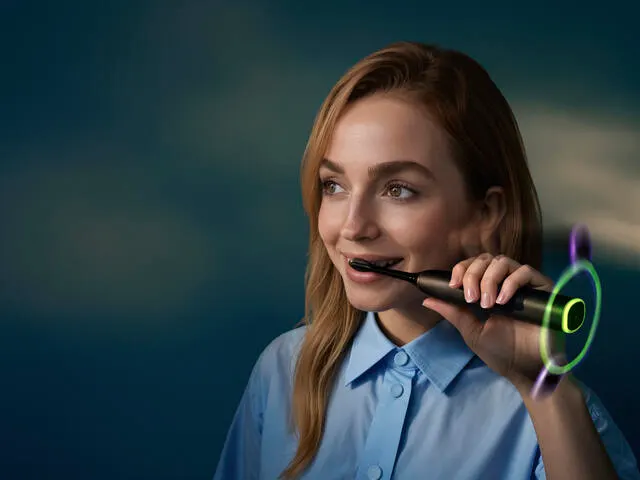 A young woman brushes her teeth using a Philips Next-Generation DiamondClean electric toothbrush.