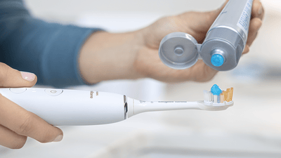 Toothpaste being put on Sonicare power toothbrush.