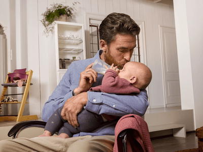 A smartly dressed man gently kisses his infant's head while feeding milk using a Philips Avent baby bottle.