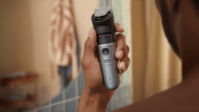 Product close-up of a black and grey Philips beard trimmer being held by a guy facing his back towards the camera.