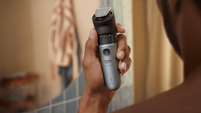 Product close-up of a black and grey Philips beard trimmer being held by a guy facing his back towards the camera.