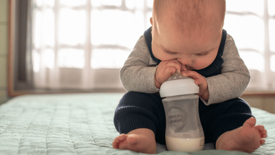 Un bébé est assis sur une surface douce de couleur vert sarcelle et boit dans un biberon Philips Avent.