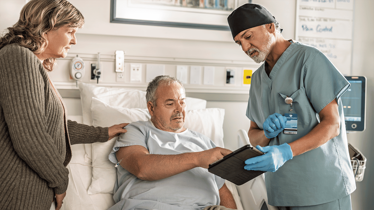 A patient in a hospital gown is seated on an examination bed. Two healthcare providers are present — one appears to hold a clipboard or document. The calm collaborative scene conveys reassurance and clinical professionalism, contextualising the endoscopy section.