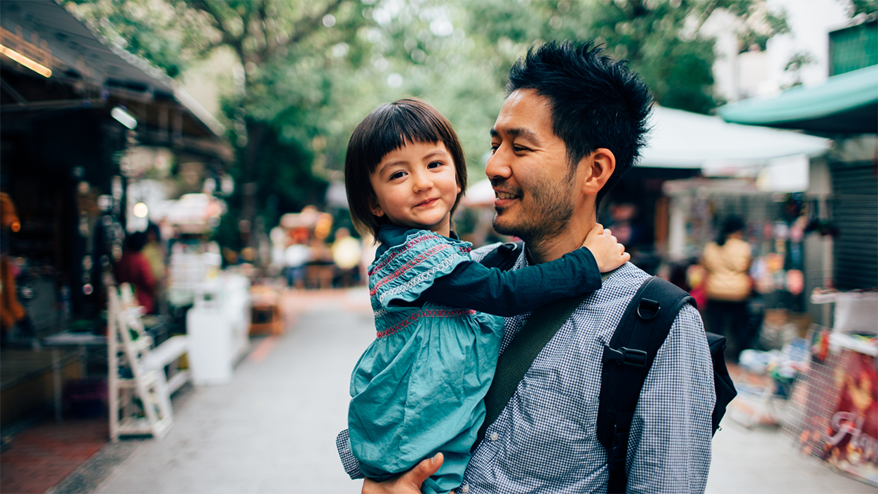 An adult and a young child are photographed together in a warm outdoor urban setting, conveying connection, emotional wellbeing, and everyday life.