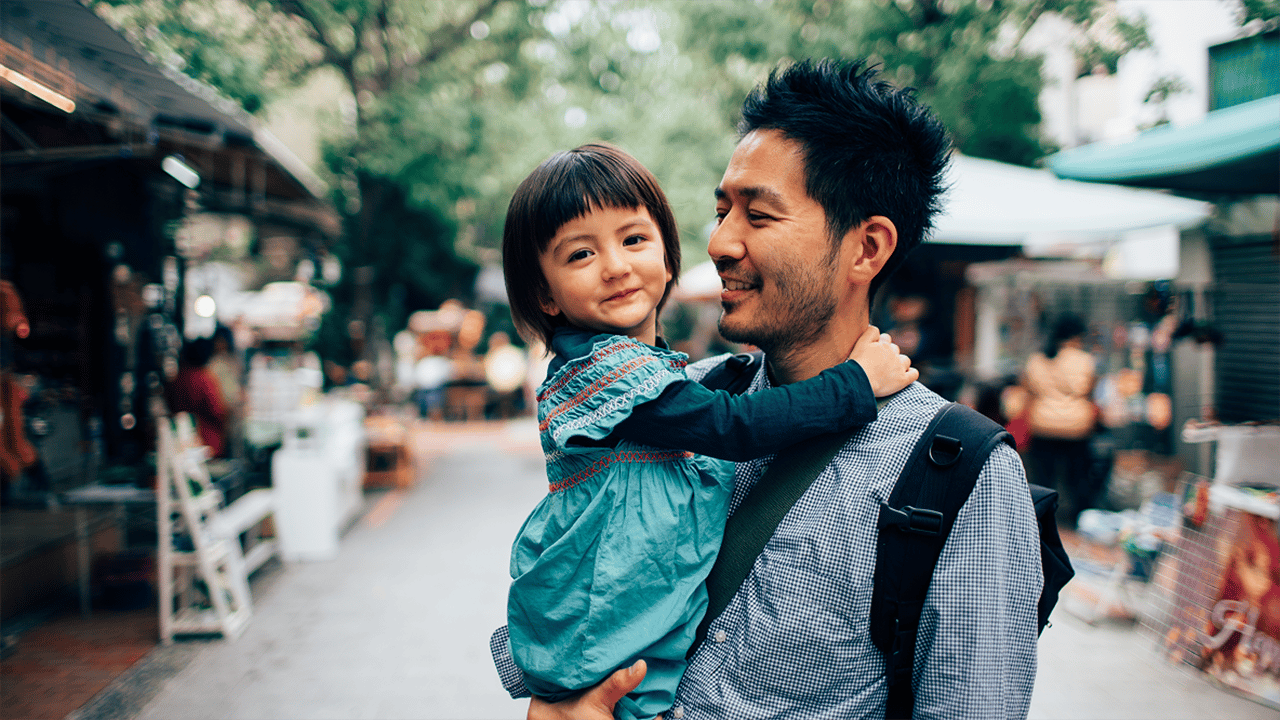 An adult and a young child are photographed together in a warm outdoor urban setting, conveying connection, emotional wellbeing, and everyday life.
