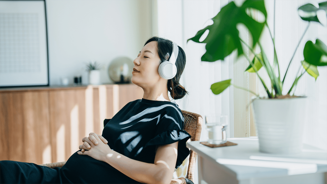 A pregnant woman is photographed in what appears to be a relaxed home or personal wellness environment, conveying calm and personal wellbeing. Navigational thumbnail for the Fertility, Pregnancy and Relationships FAQ section.