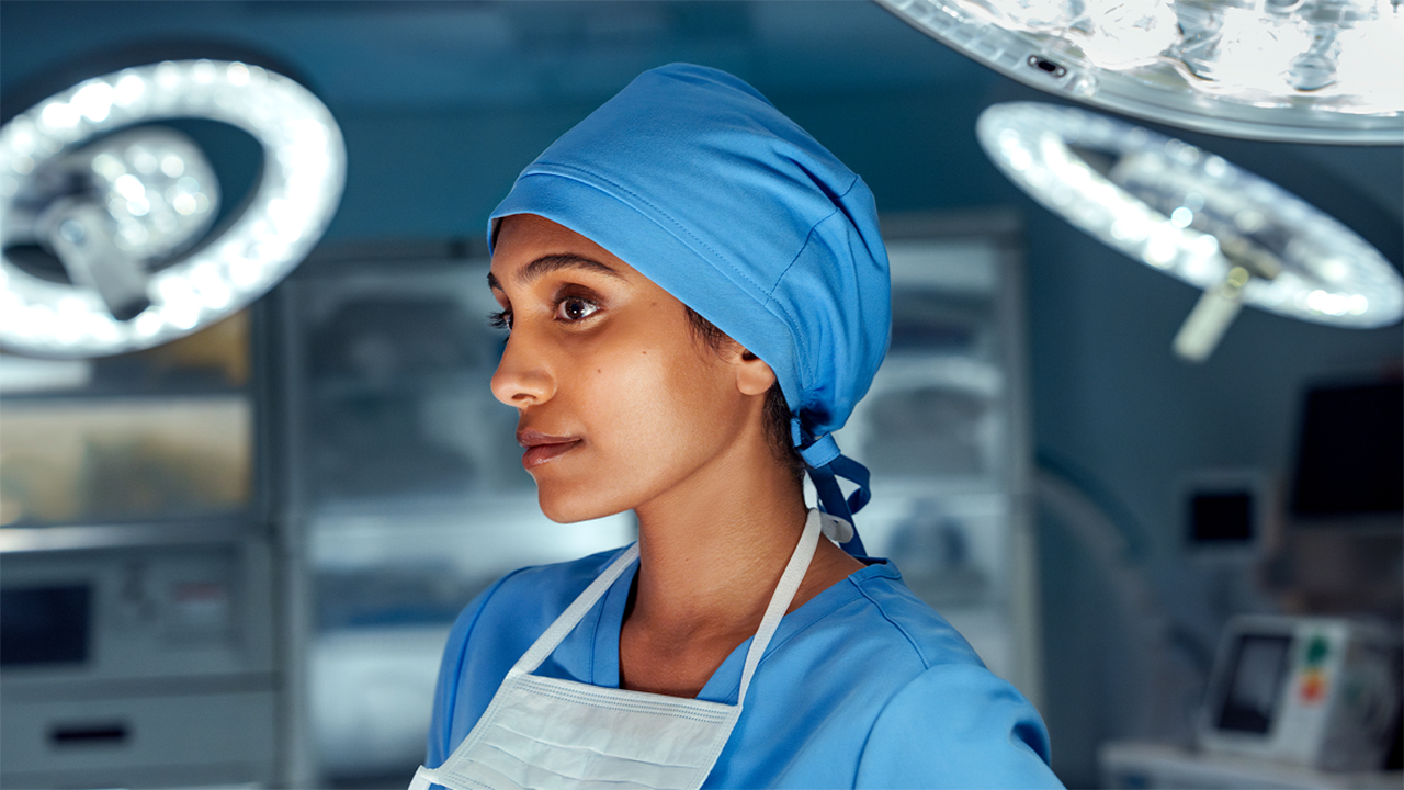 A healthcare professional wearing blue surgical scrubs and a surgical cap is photographed in what appears to be a clinical or operating theatre environment, representing surgical treatment for Crohn's disease.