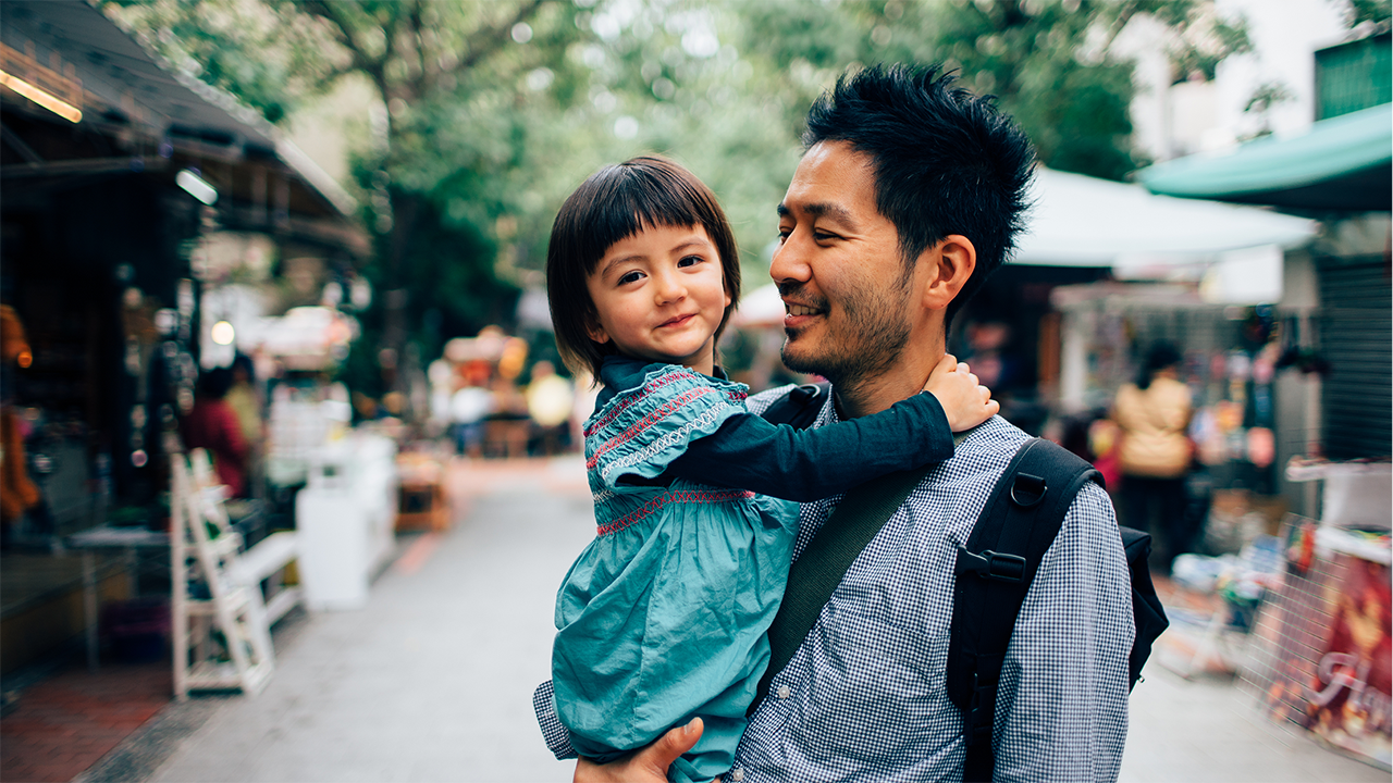 An adult carries or holds a young child in a close affectionate pose. The warm natural setting suggests outdoor or ambient natural lighting. Accompanies content about transmural healing in Crohn's disease — the deepest bowel-wall healing stage — evoking stability, care, and an active daily life.