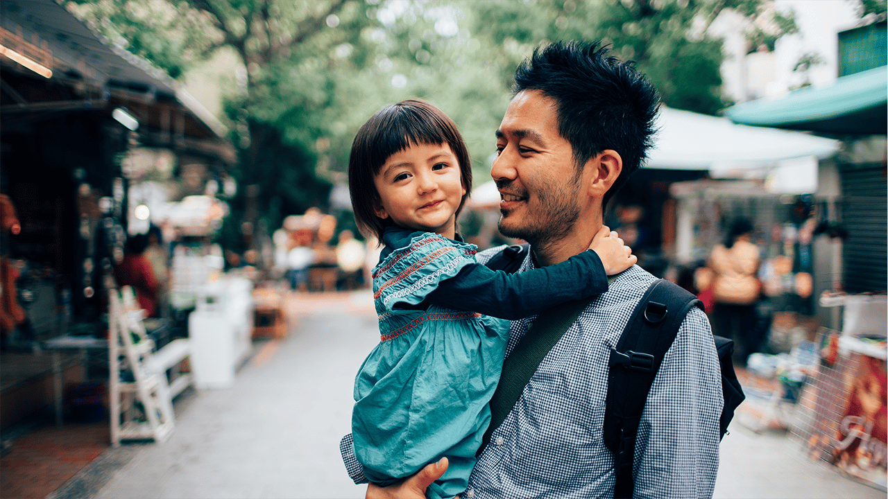 An adult carries or holds a young child in a close affectionate pose. The warm natural setting suggests outdoor or ambient natural lighting. Accompanies content about transmural healing in Crohn's disease — the deepest bowel-wall healing stage — evoking stability, care, and an active daily life.