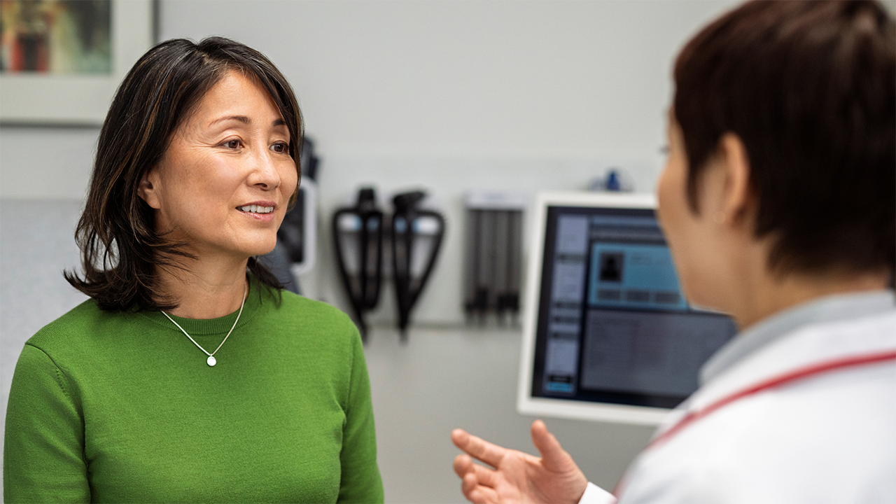 A patient and doctor engage in an attentive and purposeful exchange in a professional, clinical environment, suggesting the kind of confident, prepared conversation a patient can have when they know the right questions to ask.