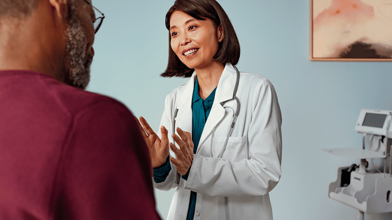 A female healthcare professional in a white coat and stethoscope smiles during a patient consultation. The positive, reassuring clinical exchange supports the physical examination step in the ulcerative colitis diagnosis section.