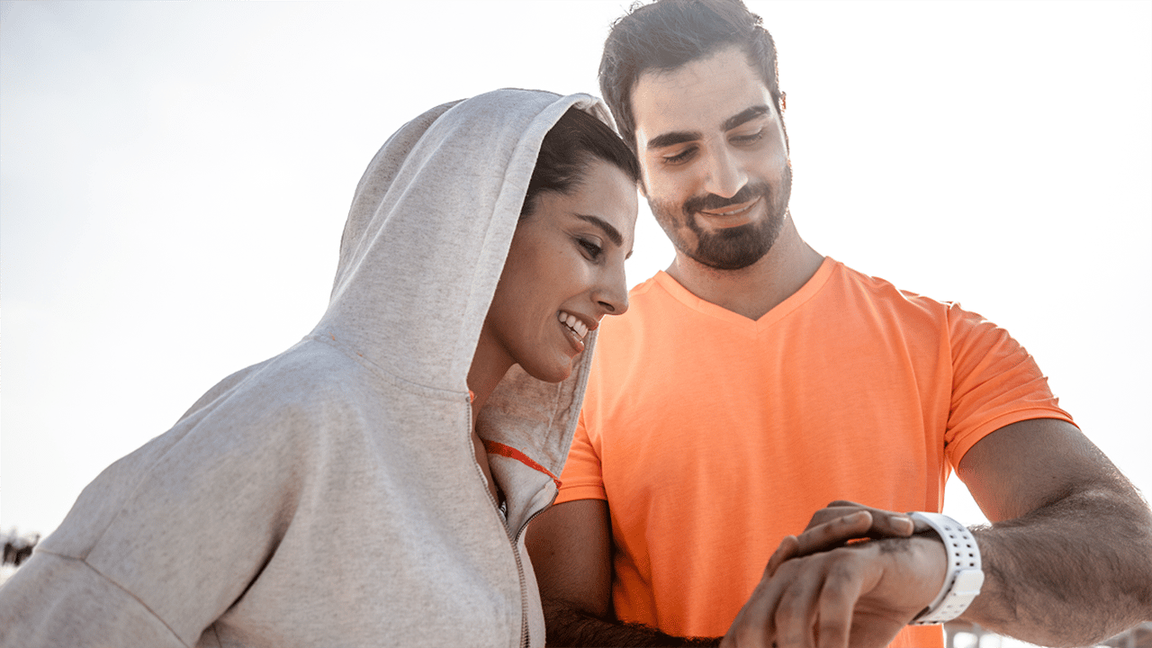 A smiling couple sharing a light-hearted moment while exercising together, reflecting on their progress via a smartwatch. Her confident demeanour represents the optimistic theme of symptom control and ongoing monitoring in this FAQ section.