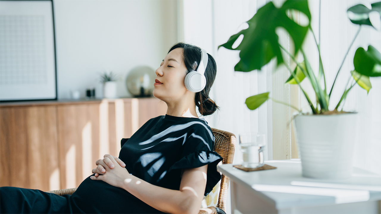 A smiling pregnant woman relaxing at home, conveying energy and positivity. The image supports the fertility, pregnancy, and family section, suggesting life aspirations and physical wellbeing.