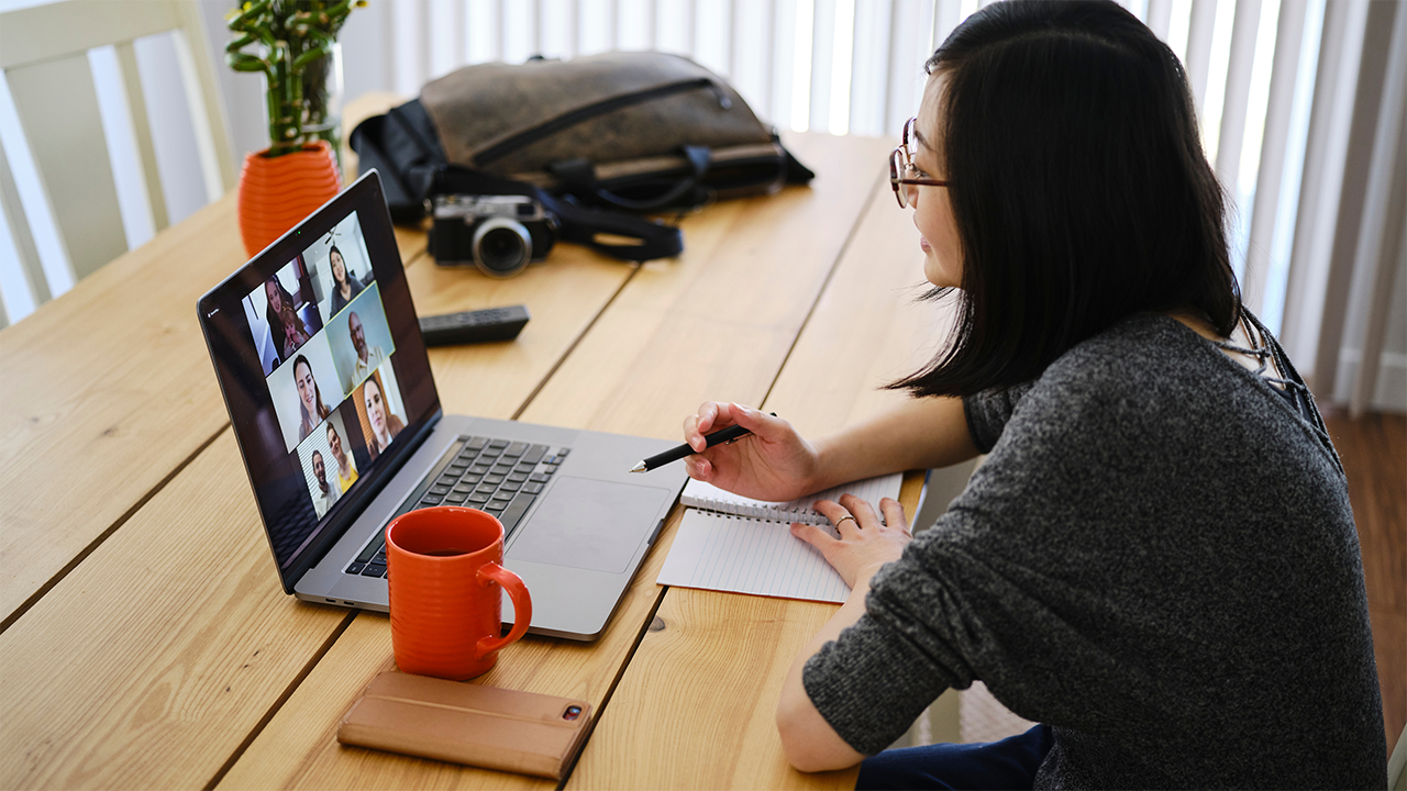 A person sits attentively at a table or desk reviewing information on a laptop or printed materials in a relaxed, home-like environment, reflecting the independent process of understanding treatment options before a medical appointment.