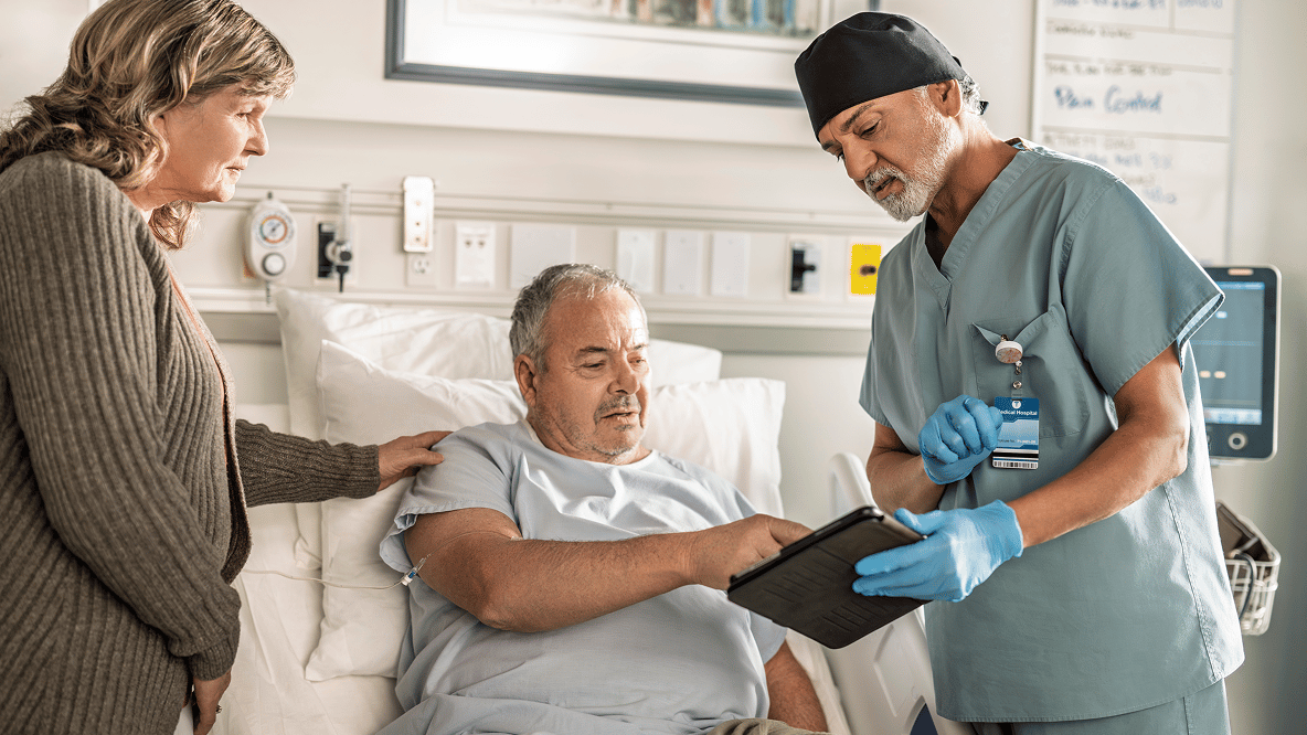 An older person is photographed alongside a healthcare professional or carer in what appears to be a warm consultation or care environment, representing the treatment relationship and long-term care goals for Crohn's disease.
