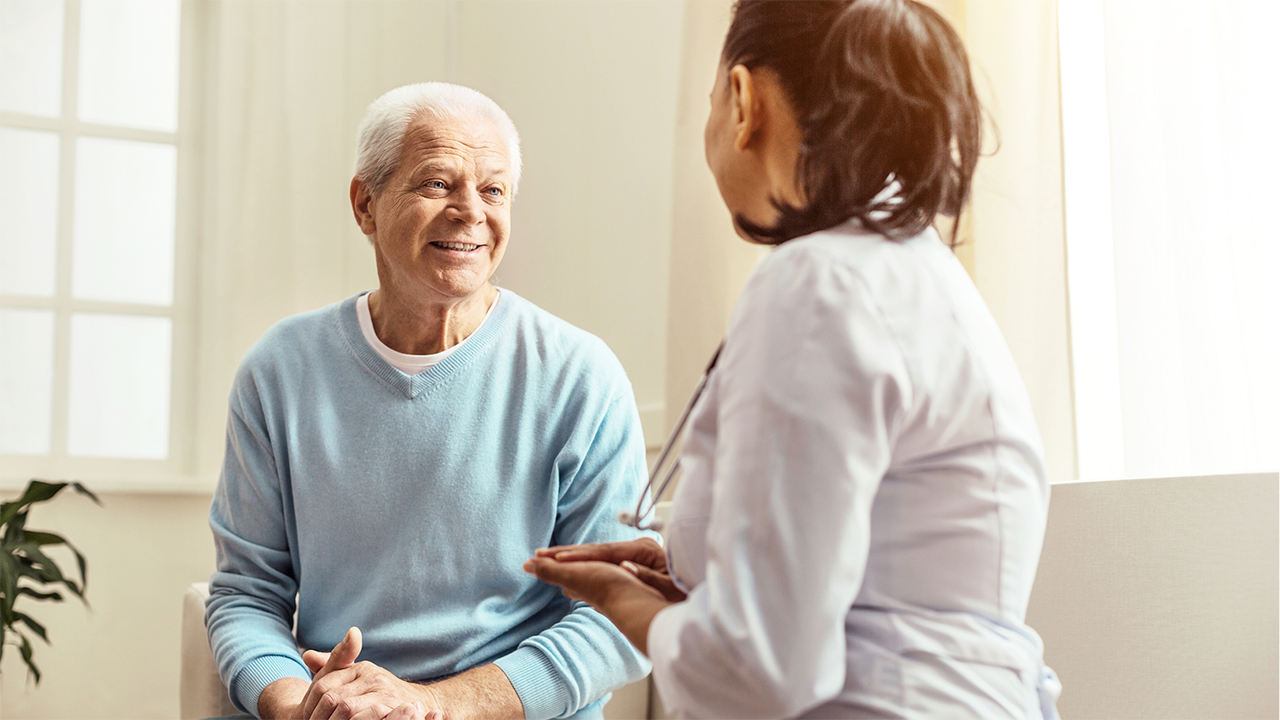An older patient and a younger doctor sit facing each other in a softly lit interior space. Their postures suggest an engaged and trusting conversation. The image accompanies copy about symptomatic remission as the first recognised milestone.