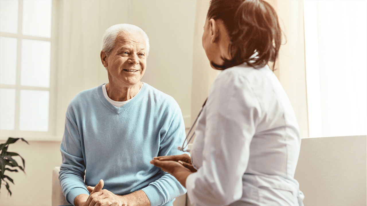 An older patient and a younger doctor sit facing each other in a softly lit interior space. Their postures suggest an engaged and trusting conversation. The image accompanies copy about symptomatic remission as the first recognised milestone.