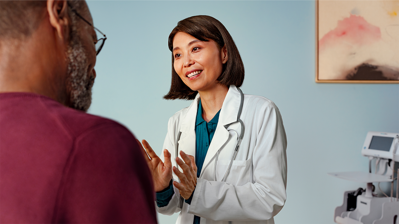 A female healthcare professional in a white coat and stethoscope smiles during a patient consultation. The positive, reassuring clinical exchange supports the physical examination step in the Crohn's disease diagnosis section.