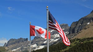 Canada and U.S. flags with snowy mountain in background