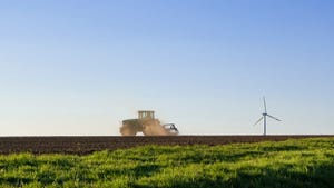 Tractor cultivating field with wind turbine on horizon
