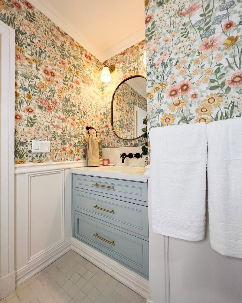 Wallflower Day wallpaper in a bathroom setting with blue cabinetry, white wall panelling and a circular mirror on the wall
